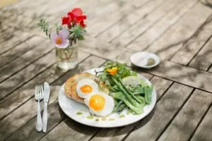 Brunch with eggs, greens on outdoor wooden table.