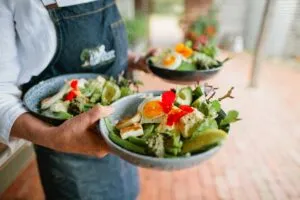 Person holding plates of fresh garden salad.