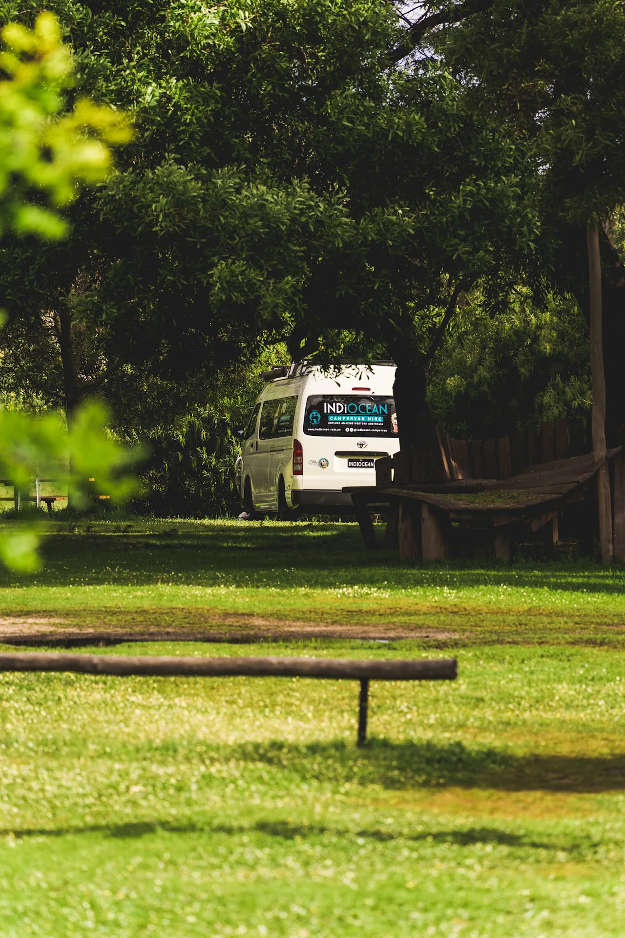 Camper van parked under lush green trees.