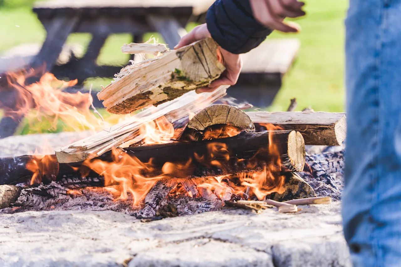 Person adding wood to campfire outdoors.